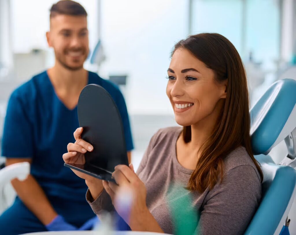 Dental patient smiling at her reflection in a handheld mirror