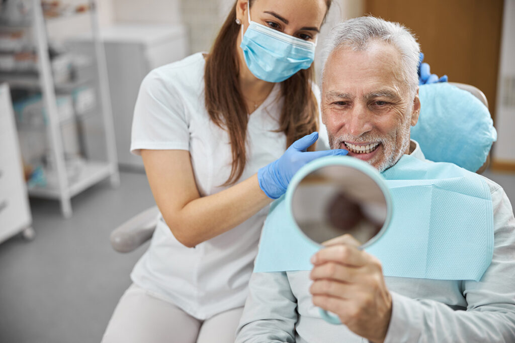 Dentist helping an older patient view his smile in a mirror