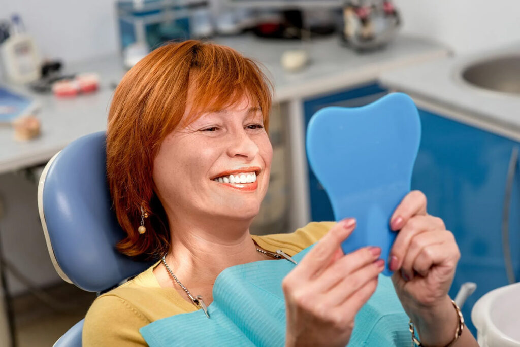 Dental patient smiling at her reflection in a handheld mirror